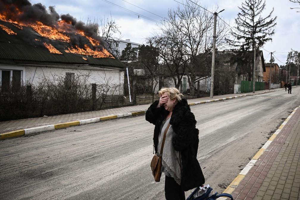 0403 - Uma mulher reage em frente a uma casa em chamas bombardeada na cidade de Irpin nos arredores de Kiev nesta sexta 4 Mais de 12 milho de pessoas fugiram da Ucrnia para pases vizinhos desde que a Rssia lanou sua invaso em grande escala em 24 de fevereiro segundo a ONU Foto Aris MessinisAFP